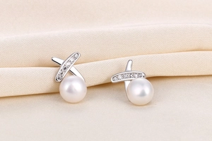 Macro shot of S925 silver pearl stud earrings with crisscross zircon design on silk