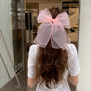 Close-up of a large pink organza bow hair clip on long wavy hair with a soft romantic look
