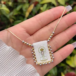 Detail of 18K gold-plated necklace featuring a cartoon Virgin Mary fabric pendant with beads