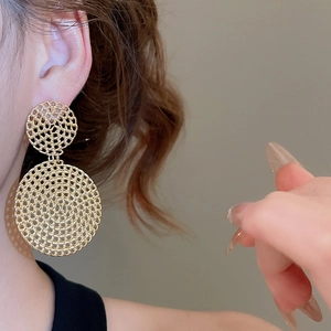 Detail of gold woven mesh round earrings showing intricate spiral metallic texture on skin