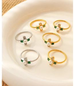 Detailed view of vintage gold rings with pearls and green gemstones on ceramic tray