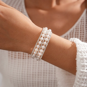 Close-up of a three-layer pearl and rhinestone cuff bracelet on a woman's wrist