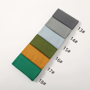 Flat lay detail showing six folded cotton linen scarves in various solid colors on white back