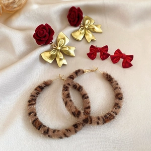 Detailed set of leopard print earrings and red bow studs on beige satin fabric