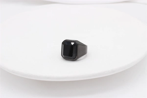 Detail of a minimalist men's black stainless steel ring with an octagonal gemstone on a white plate