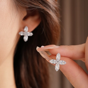 Vue détaillée des boucles d'oreilles trèfle en argent avec zircons portées et tenues en main