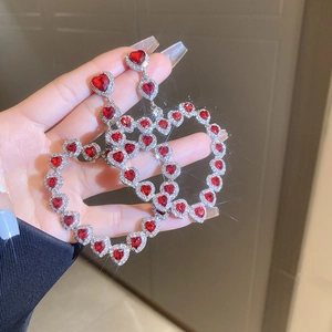 Detailed view of oversized silver-tone heart earrings with red crystals and sparkling rhinestones