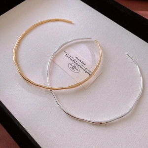 Detailed top view of gold and silver minimalist wavy open chokers on a white display tray