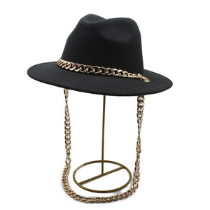 Classic black fedora hat featuring a bold gold chain band on a minimalist metal stand