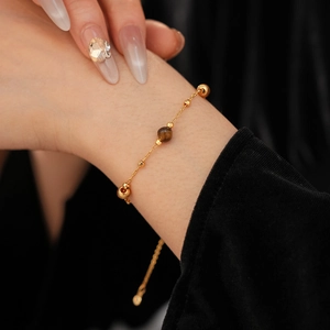 Detail of gold-plated bracelet featuring a natural tiger eye bead on a female wrist