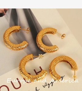 Detailed view of gold C-shaped earrings with hammered texture on vintage magazine background