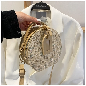 Detail of round straw bag featuring delicate colorful floral embroidery and smooth zipper