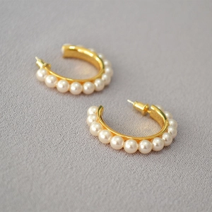 Macro detail of elegant gold plated C-shaped earrings with inlaid white pearls