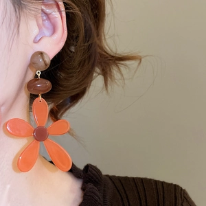 Detailed close-up of orange resin flower tassel earrings worn by a model in warm light