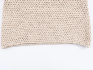 Detailed macro view of the thick beige chunky knit fabric and ribbed hem texture