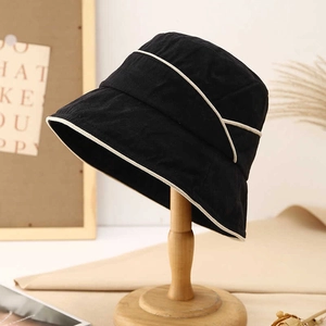 Minimalist black cotton sun hat with beige piping detail displayed on a wooden stand