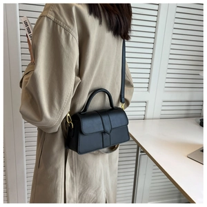 Detail of a black PU leather crossbody bag with gold hardware worn over a beige coat