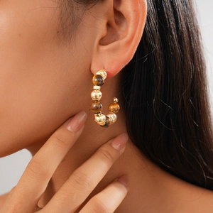 Close-up of 16K gold-plated C-shaped earrings with tiger eye beads on a model
