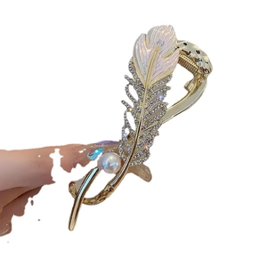 Elegant gold feather hair claw clip with pearls and rhinestones shown in a hand