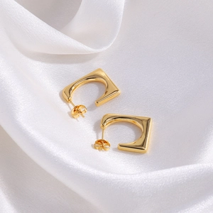Detail of gold square C-shaped hoop earrings on elegant white silk fabric background