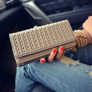 Dettaglio di un portafoglio lungo beige con borchie dorate tenuto in mano in un ambiente casual