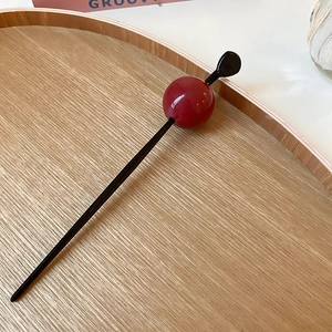 Detail view of a minimalist black hair stick with a polished red resin bead on wood