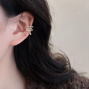Close-up of golden bow ear cuff with pearls and zircons worn on ear for non-pierced style