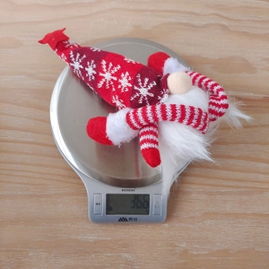 Christmas gnome doll with snowflake knit hat being weighed on a digital scale