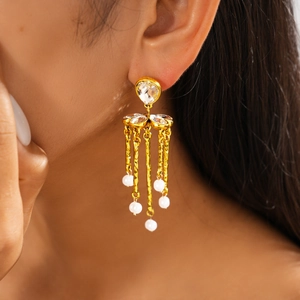 Close-up of gold drop earrings with clear stones and pearl tassels worn by a model