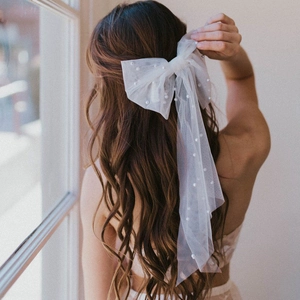 Detail of white tulle bow hair clip with pearls and long ribbons on wavy brown hair