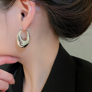 Close-up of a model wearing polished silver-toned oval drop earrings with a sleek finish