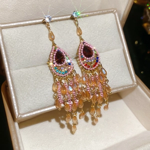 Detail view of gold drop earrings with red pear stone and sparkling crystal tassels