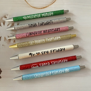 Close-up of seven colorful glitter pens with festive holiday weekday engravings
