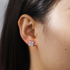 Macro shot of silver stainless steel cutout witch knot stud earring worn on ear