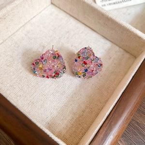 Macro view of heart-shaped pink stud earrings with colorful glitter in a linen box