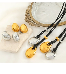 Detail of gold and silver hollow teardrop earrings and necklaces on textured stone