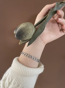 Detail view of a silver link chain bracelet worn on wrist with retro floral props