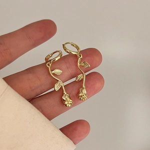 Detailed close-up of long gold-plated rose earrings with stem and leaf accents