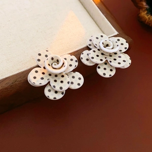 Gros plan de boucles d'oreilles fleurs en acrylique blanc avec pois noirs sur plateau