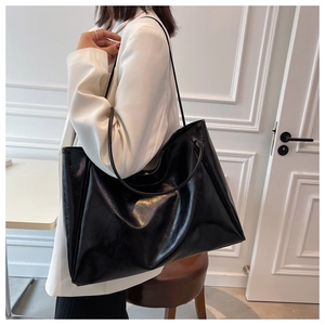 Detailed view of the large black faux leather tote bag worn over a white blazer