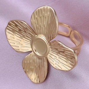 Macro d'une bague fleur dorée aux pétales texturés sur fond de soie rose délicat