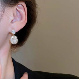 Close-up of double-layered gold earrings with oval clear zircons on a female model