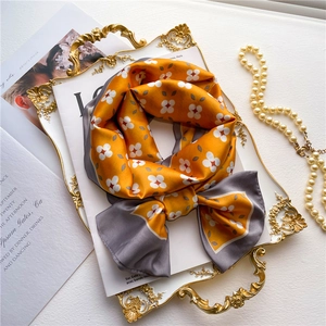 Double-sided yellow and grey floral silk scarf tied in a bow on a gold tray