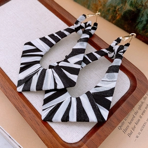 Close-up of geometric earrings with black and white striped fabric wrap on wooden tray