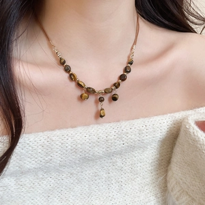 Detail of beaded tiger eye tassel necklace on model with golden metal hardware