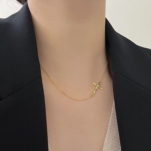 Detail of a gold irregular cross necklace worn by a model in a black suit