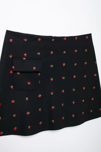 Détail d'une mini-jupe noire avec broderies de fraises rouges et une poche sur le côté