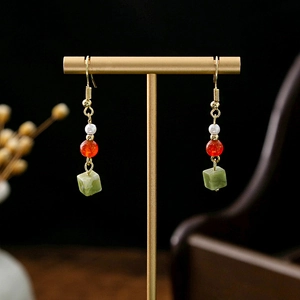Detail of vintage earrings with red beads, green jade pendant, and gold hollow flowers