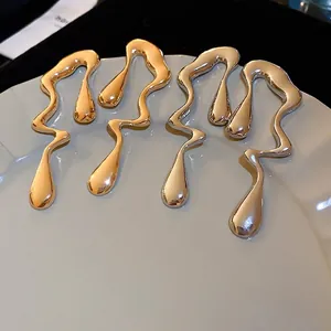 Modern irregular liquid metal drop earrings in gold and silver finish on a ceramic plate
