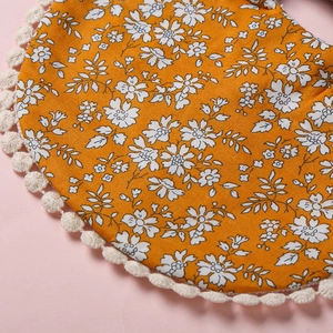 Gros plan d'un bavoir bébé floral jaune en coton avec bordure en dentelle à pompons